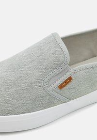 Szürke slip-on cipők texturált vászon felsőrésszel, kontraszt színű világosbarna bőr díszítéssel és fehér gumi talppal.