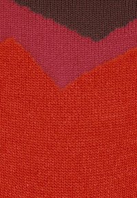 Gebreide stof met een chevronpatroon in donkerbruin, magenta en helderrood, met een gedetailleerde brei-textuur.