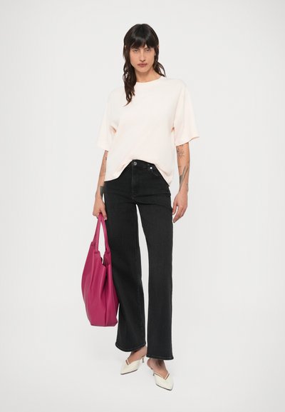 Camiseta de manga curta cor-de-rosa claro, jeans pretos de cintura alta, segurando uma mala rosa choque texturizada. Sapatos brancos apontados completam o conjunto.