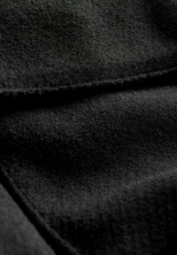 Sort uldstof med en blød, mat tekstur. Nærbillede viser dens tætte fibre og glatte overflade, foldet for at afsløre lag.