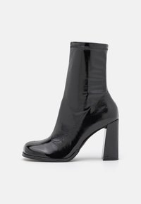Sort ankelstøvle med en glansfuld finish, der har en firkantet tå, høj blokhæl og elastiske sider for en strømlinet silhuet.