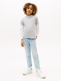 T-shirt grigio a maniche corte indossato sopra una camicia bianca a maniche lunghe, abbinato a jeans azzurri chiari e sneakers bianche. Look casual con orli arrotolati.