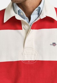 Rood-wit gestreepte polo shirt met een kraag, knoopsluiting en geborduurd logo. Zachte stof met een gladde textuur.