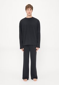 Zwart loungewear set bestaande uit een langmouwen crew neck top en losse broek, gemaakt van zachte stof met een gladde textuur.