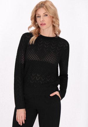 Pulover negru cu modele texturate și designuri în formă de V. Mâneci lungi și tiv cu elastic. purtat cu pantaloni negri.