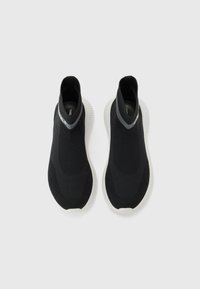 Black slip-on sneakers made of textured knit material, featuring a high ankle design and a white rubber sole with distinct tread pattern.