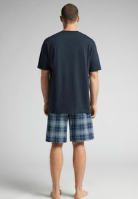 Marineblaues Baumwoll-T-Shirt mit kurzen Ärmeln, kombiniert mit blauen Karotten-Shorts, die weiße und dunkelblaue Linien aufweisen. Keine sichtbaren Logos oder Muster.