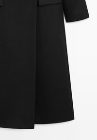 Černý kabát s padnoucím střihem, zdůrazněnými rameny, rovný řez a texturovaná tkanina pro elegantní vzhled.