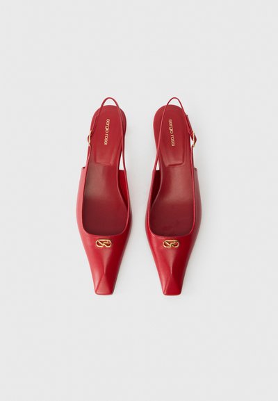 Red leather slingback heels with pointed toes and a gold logo accent. Smooth texture, minimalistic design, open heel, and flat sole.
