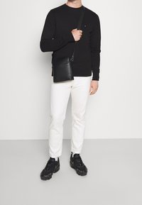 Maglietta nera a maniche lunghe, pantaloni bianchi slim-fit e sneaker nere. Borsa a tracolla in pelle nera con zip. Design semplice e moderno.