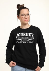 Zwarte sweatshirt met een grafische print met de tekst "JOURNEY 1983 FAITHFULLY." De stof is zacht, met ribgebreide manchetten en een ronde hals ontwerp.