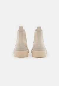 Botas de tobillo de cuero beige con textura suave, paneles laterales elásticos y suela gruesa de color crema, con una tira de sujeción en la parte posterior.