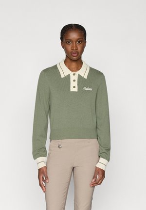 Grøn strikket sweater med en fløjlsfarvet krave, der har tre knapper og ribbede manchetter. Mærkenavnet er broderet på venstre side.