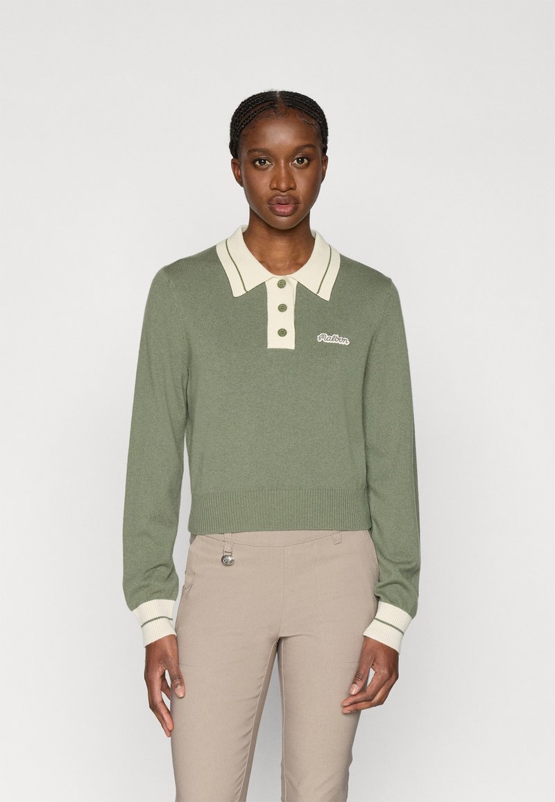 Zaļš adīts džemperis ar krēmkrāsas apkakli, ar trim pogām un ribotām piedurknēm. Zīmola nosaukums izšūts kreisajā pusē.