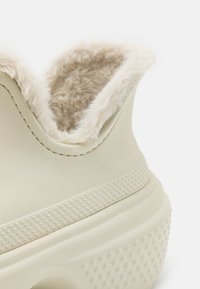 Kremowe sneakersy z teksturowaną, gumową podeszwą. Posiadają puszyste, beżowe wykończenie przy kołnierzu oraz subtelne, przeszywane detale.