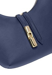 Borsa a mano in pelle testurizzata blu navy con chiusura in bronzo e due tiranti della cerniera in pelle abbinati su uno sfondo bianco.