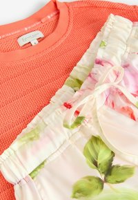 Coral knit sweater with a textured design paired with a cream-colored garment featuring floral patterns and a drawstring accent.