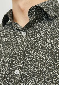 Chemise boutonnée avec un motif floral sombre, dotée d'un col, de boutons blancs et d'un tissu texturé. Le motif comprend de petites fleurs et feuilles blanches.