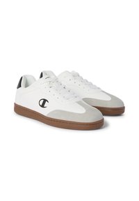 Zapatillas blancas con acentos de ante gris, suela de goma marrón y logo de marca en el costado. Diseño con cordones y detalles perforados en la parte superior.