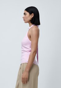 Lyserosa halterneck-topp med en tettsittende design, sideutskjæringer og en knyttet detalj på baksiden. Glatt tekstur kombinert med beige høyt liv-bukser.