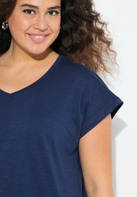 Marineblå T-shirt med V-hals, korte oprullede ærmer og et blødt, struktureret stof. Simpelt design uden mønstre eller pynt.