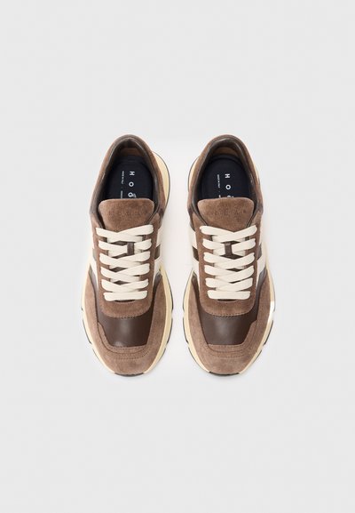 Prünt pruunidest ja beežidest seemisnahk- ja nahksneakeritest, kreemiate paeltega, vaadet ülhäält heledal taustal.