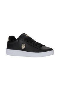 Baskets en cuir noir avec une semelle en caoutchouc blanc, dotées de lacets noirs, d'un logo en accent doré et d'une finition texturée sur le matériau supérieur.