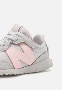 Light grey sneaker with a pink "N" logo, textured material, padded collar, and laces. Rubber sole with visible tread pattern.