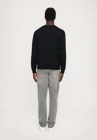 Pulover negru cu mâneci lungi, blugi gri drept, și adidași albi. Țesătura pare netedă, cu un design clasic și minimalist.