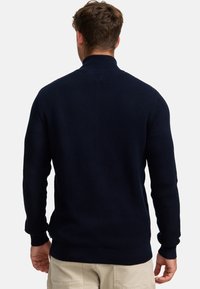 Suéter de punto azul marino con cuello alto, patrón texturizado y puños y dobladillo acanalados. Presenta mangas largas y un diseño de color sólido.