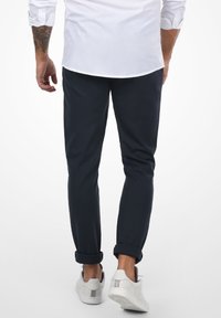 Marineblå slim-fit bukser i bomull, med oppbrettede cuffs, kombinert med hvite joggesko og en hvit skjorte synlig på toppen.