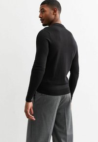 Zwarte trui met lange mouwen, gebreid en met een aansluitende snit en geribbelde zoom, gecombineerd met geruite grijze broek. De stof lijkt glad en licht van gewicht.