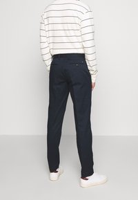 Granatowe spodnie o prostym kroju, z pasem z przelotkami na pasek oraz dwoma tylnymi kieszeniami zapinanymi na guziki.