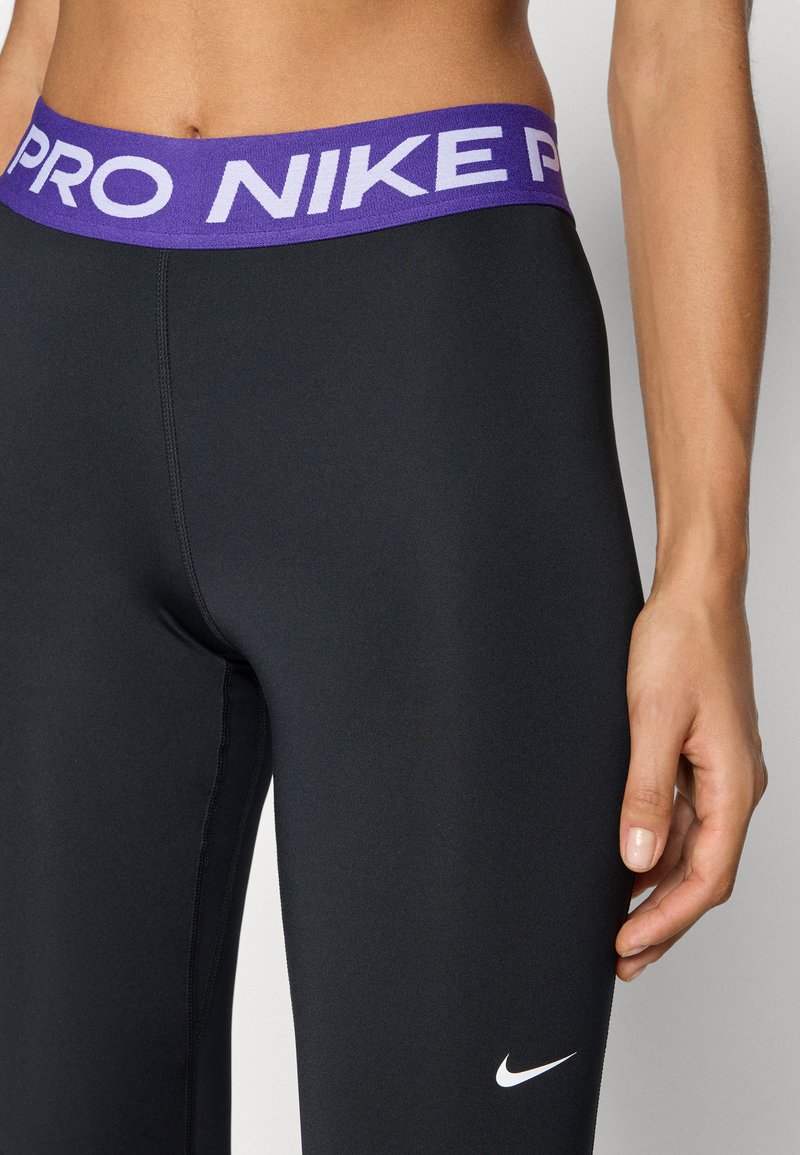 Leggings de sport noirs avec une large ceinture violette arborant les mots "PRO" et "NIKE" en blanc, en tissu lisse, et un petit logo Nike blanc.