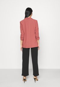 Blazer amaranto con maniche arrotolate, design strutturato e taglio dritto, abbinato a pantaloni larghi neri e tacchi aperti.