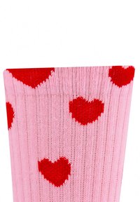 Chaussettes jusqu'aux genoux en tricot rose pâle, présentant une texture côtelée et des motifs de cœurs rouges sur toute la surface.