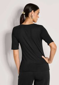 Zwart kortmouwtop met een ronde hals, gladde textuur en een getailleerd ontwerp, getoond vanuit de achterkant, gecombineerd met zwarte kleding.