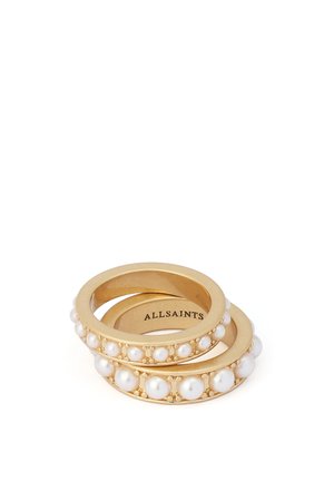 Deux bagues en or avec des perles blanches incrustées, empilées, affichant le nom de la marque "ALLSAINTS" à l'intérieur d'une bague.
