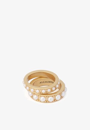 Deux bagues en or avec des perles blanches incrustées, empilées, affichant le nom de la marque "ALLSAINTS" à l'intérieur d'une bague.