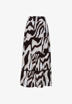 Nainen pukeutunut pliseerattuun hameeseen, jossa abstrakti ruskea, beige ja valkoinen kuvio, käsi rentosti hameen taskussa, valkoinen yläosa näkyvissä.