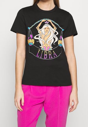 T-shirt noir avec une illustration d'une femme aux cheveux blancs ondulés tenant une balance équilibrée, avec le mot « BALANCE » en lettres colorées en dessous.