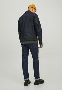 Veste en denim foncé au style classique, dotée d'un col, de détails en boutons et de deux poches arrière. Associée à un jean foncé et des bottes marron.