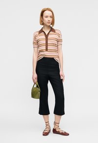 Ριγέ πόλο μπλούζα με καφέ γιακά και κουμπιά, συνδυασμένη με μαύρο φαρδύ παντελόνι και καφέ δερμάτινα παπούτσια με κορδόνια· κρατώντας μια πράσινη τσάντα.