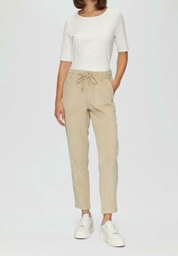 Beige kordflorsbyxor med dragsko i midjan, sidofickor och smalare ben, kombinerade med en vit ribbad kortärmad topp och vita sneakers.
