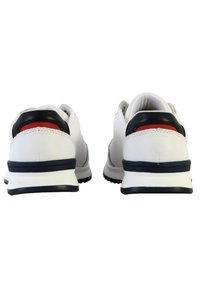 Baskets blanches avec une finition en cuir lisse, accents navy, détails rouges sur le talon et semelles épaisses texturées. Design à tige basse.