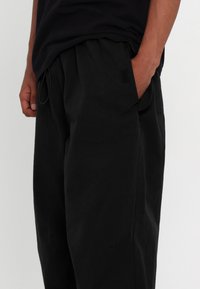 Czarne, luźne spodnie w stylu relaxed-fit z teksturowanej tkaniny, elastycznym paskiem w talii, bocznymi kieszeniami oraz małym akcentem z logo na udzie.