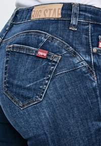 Tamsiai mėlyni džinsai iš nugaros, su Big Star prekės ženklo etikete ant kišenės ir odiniu ženkliuku ant juosmens.