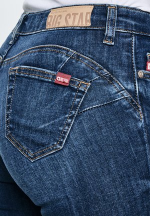 Tumesiniste teksade tagumine vaade, millel on taskul Big Star'i kaubamärgi silt ja vöökohal nahast etikett.