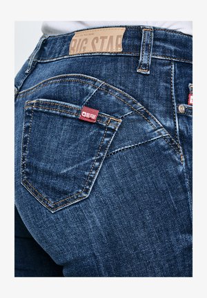 Tumesiniste teksade tagumine vaade, millel on taskul Big Star'i kaubamärgi silt ja vöökohal nahast etikett.