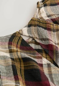 Chemise à carreaux avec des couleurs noir, or, bourgogne et crème ; présente un col en U et un tissu léger et texturé.